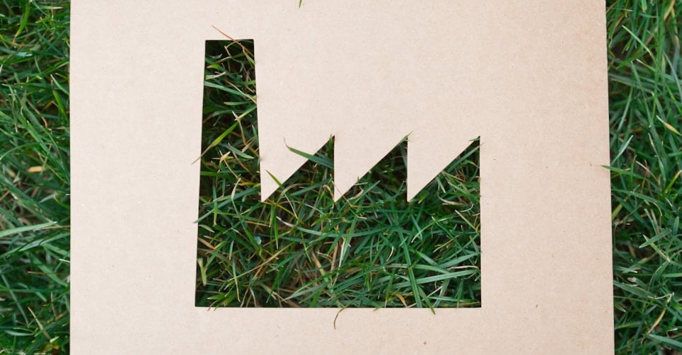 Illustrasjon - fabrikk-symbol klippet ut i papp som ligger på gress